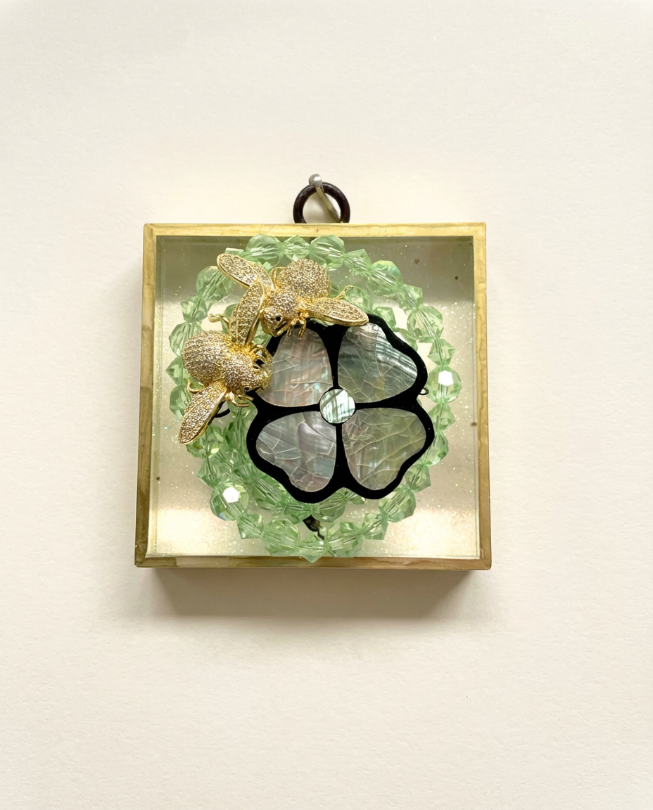 Decorative art piece with green beads, bees, and black clover design in a gold frame.