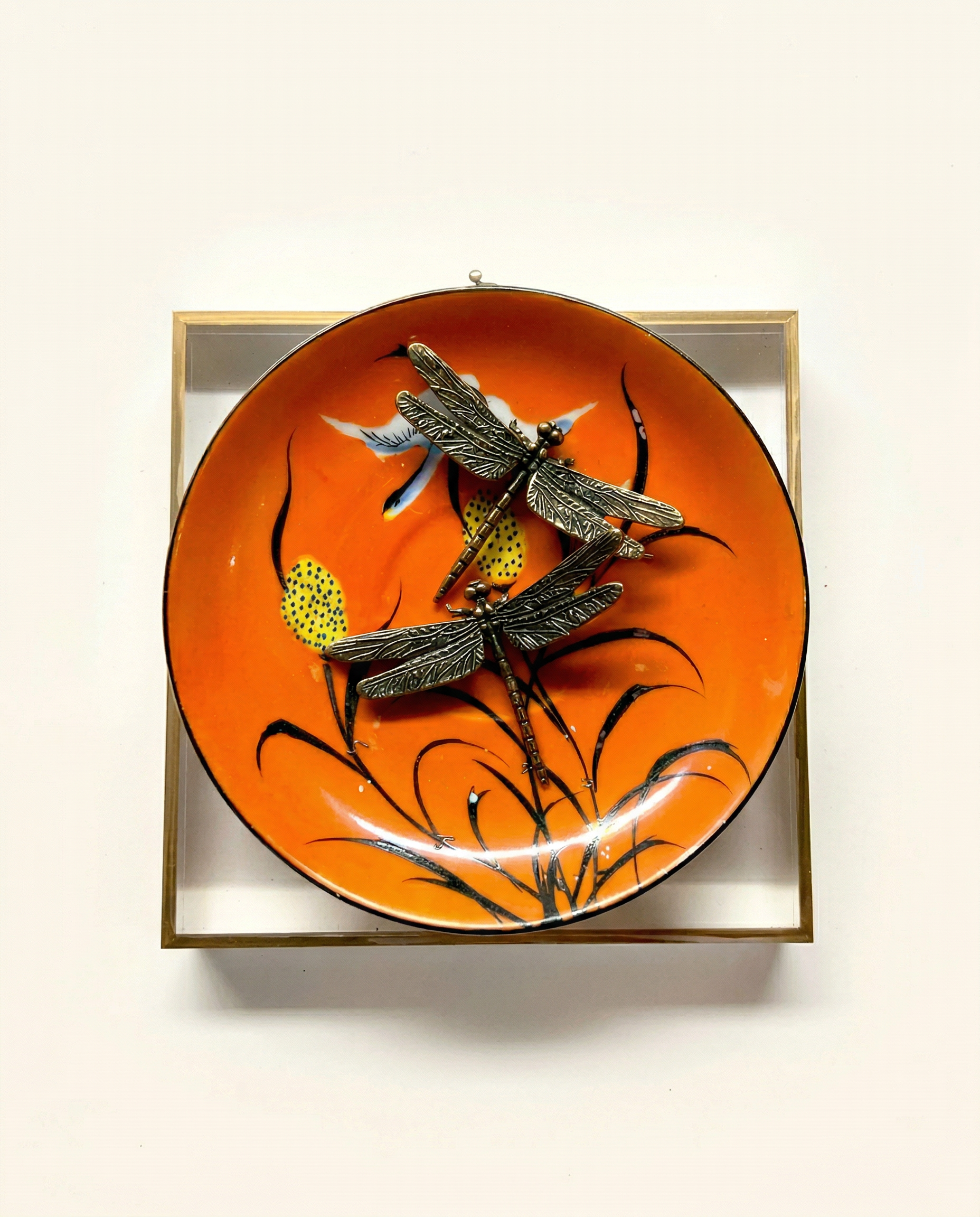 Decorative plate with dragonfly design on an orange background on acrylic frame background 