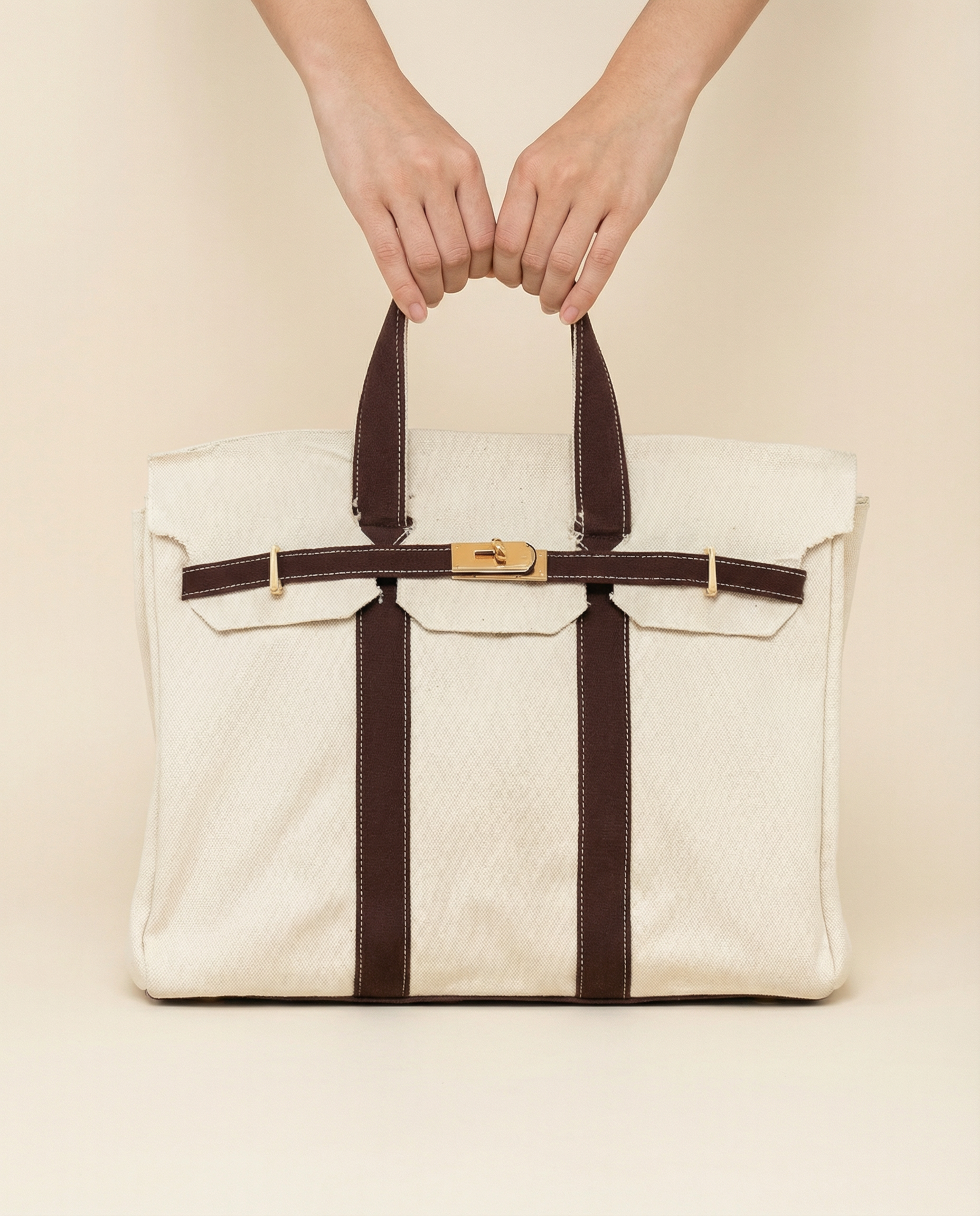 White bag with brown straps held by a person against a beige background
