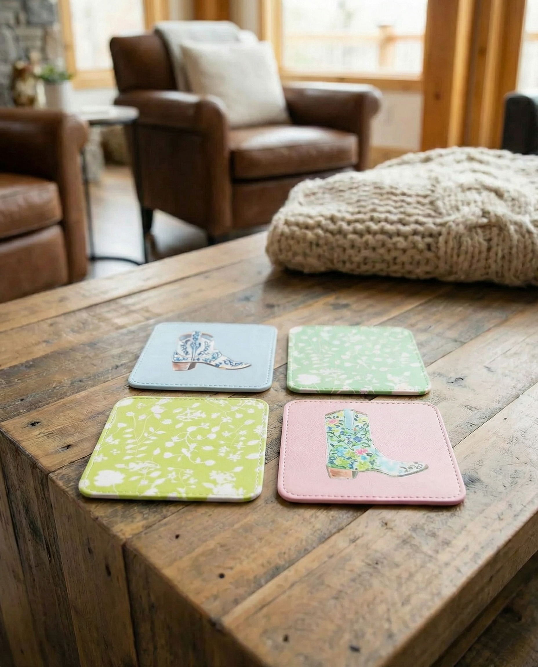 Four rodeo cowboy boot print coasters with designs on a wooden surface in a cozy living room.