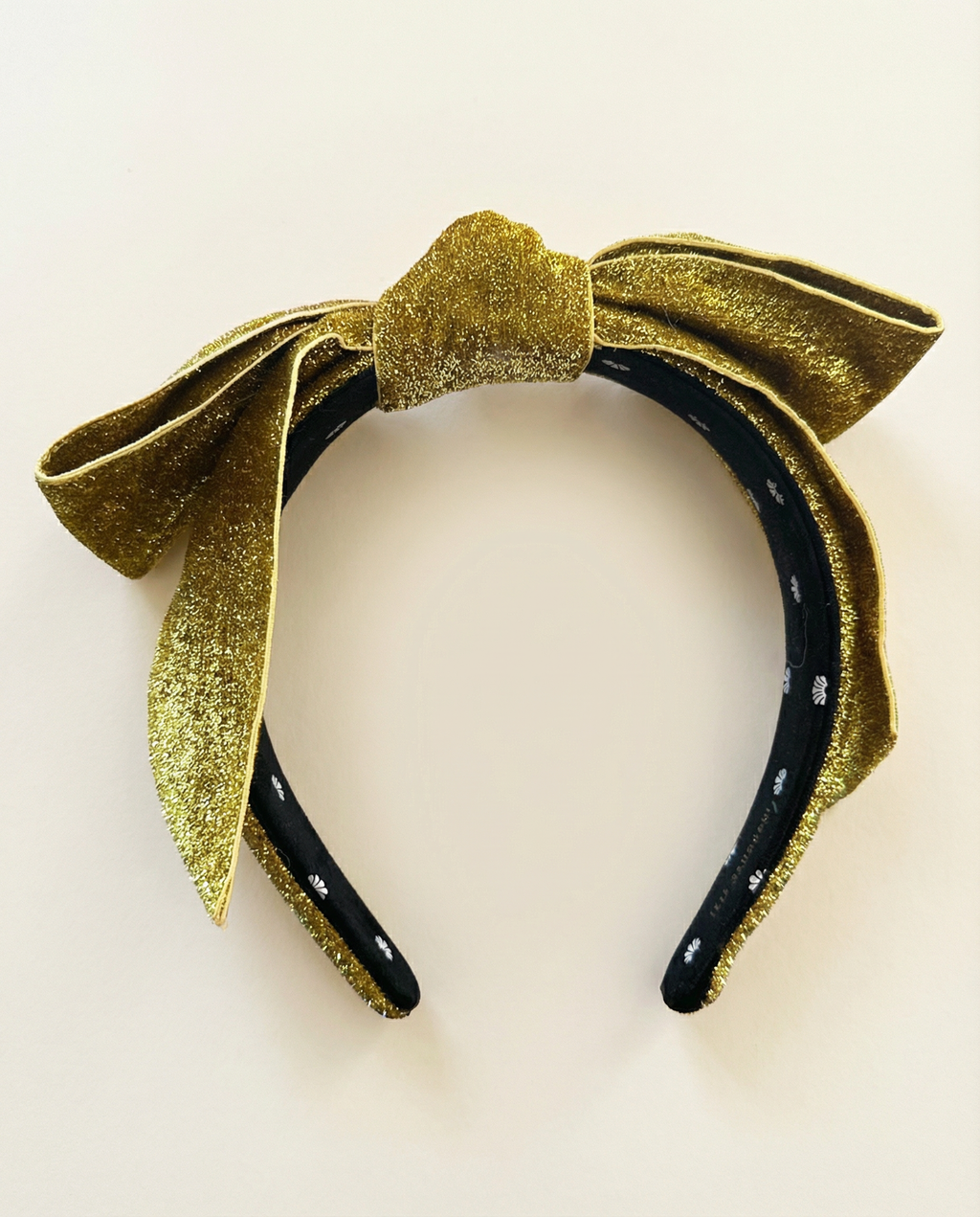 Gold and black headband with a large bow on a light beige background
