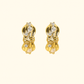 Pair of gold earrings with clear gemstones on a beige background