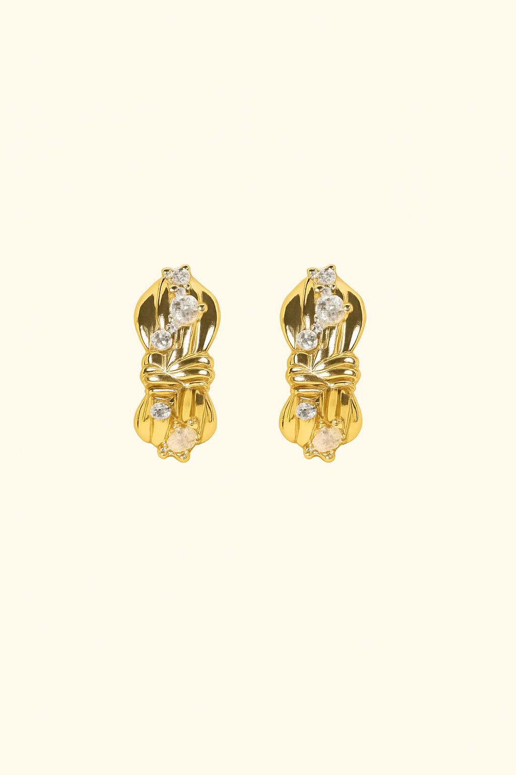 Pair of gold earrings with clear gemstones on a beige background