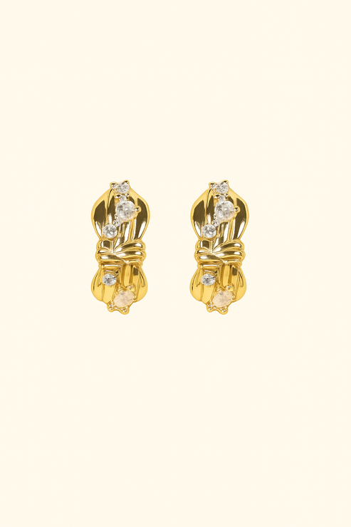 Pair of gold earrings with clear gemstones on a beige background