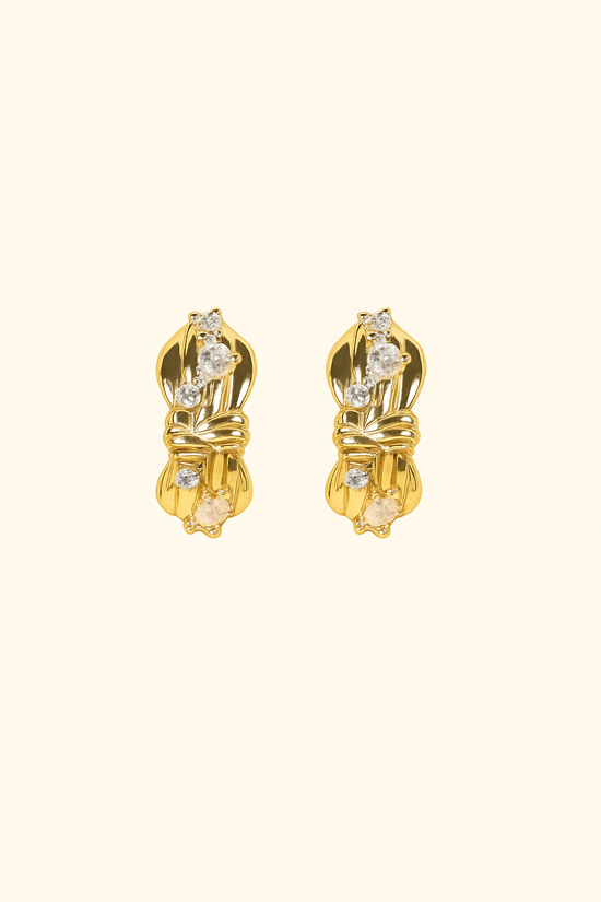 Pair of gold earrings with clear gemstones on a beige background