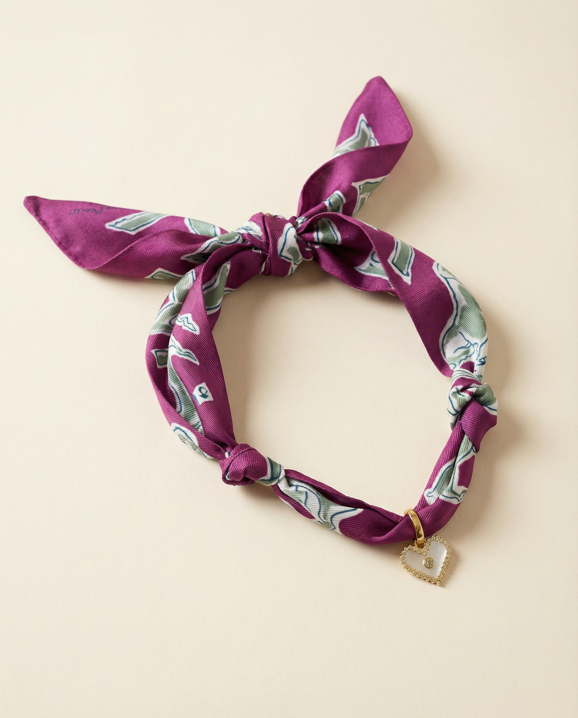 Purple patterned scarf necklace with a heart charm on a beige background