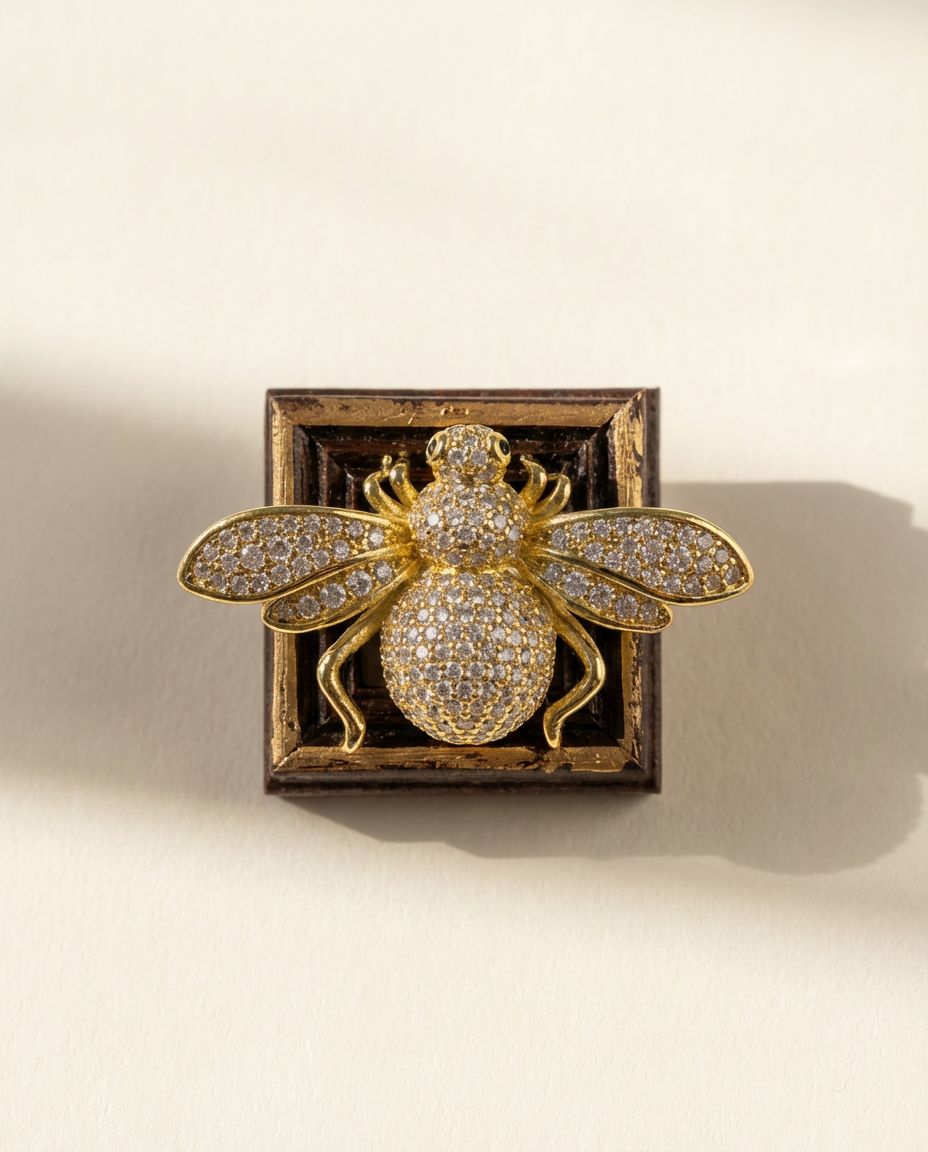 Gold bee-shaped brooch with gemstones in a decorative frame on a beige background