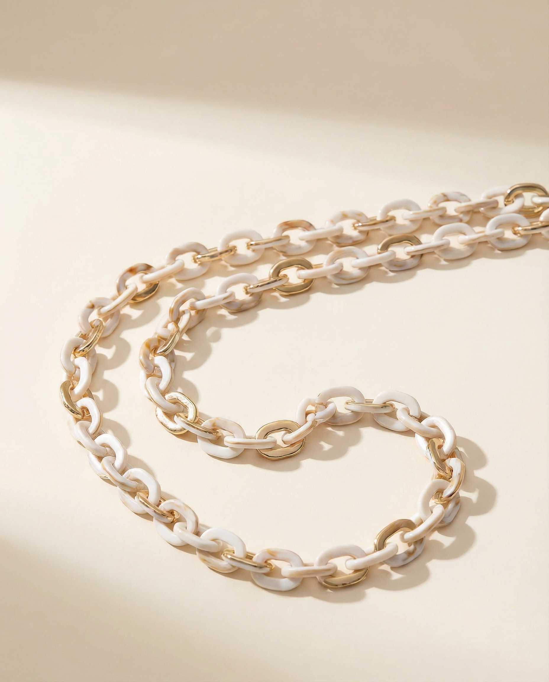 Gold and white chain iPhone strap on a beige background