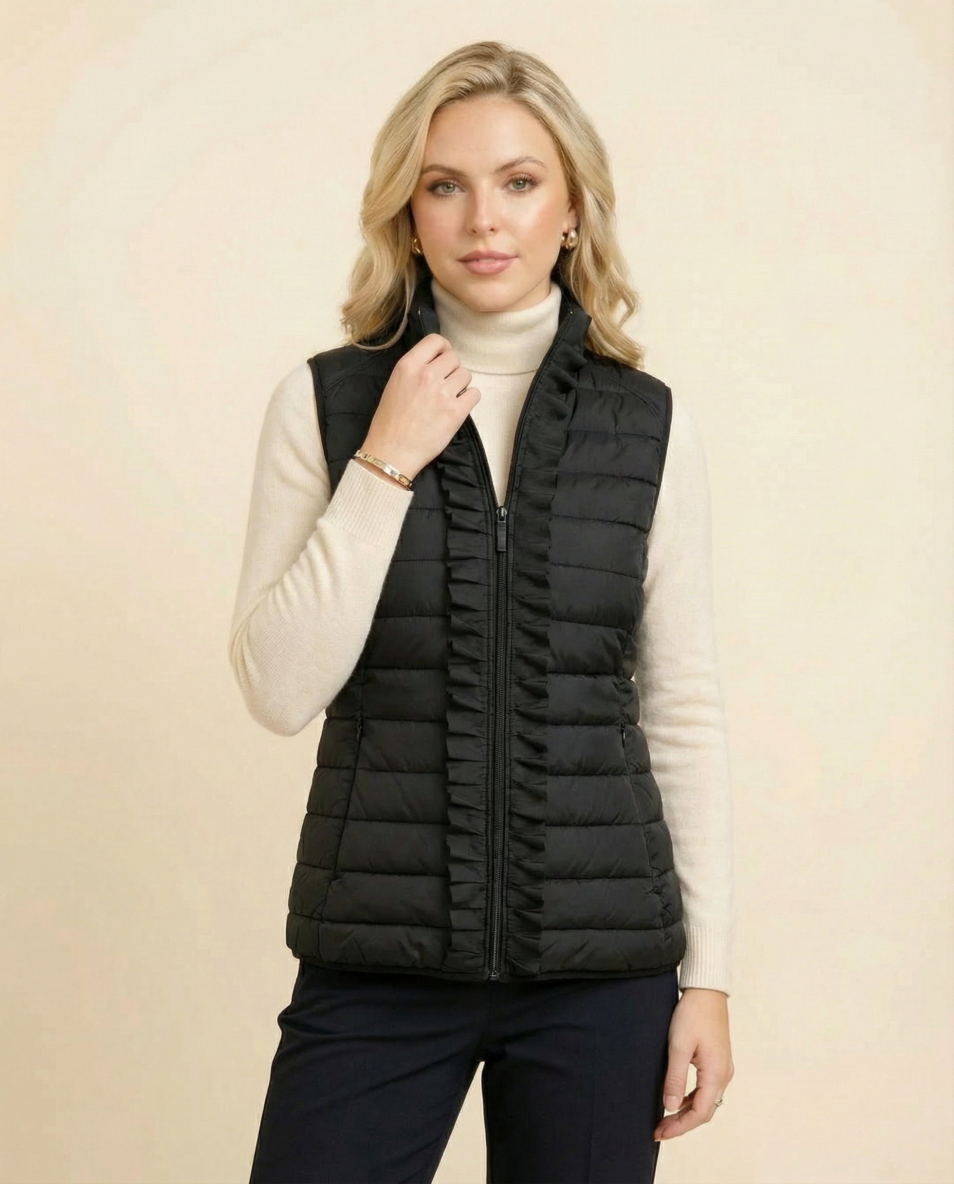 Woman wearing a black puffer vest over a white turtleneck on a beige background