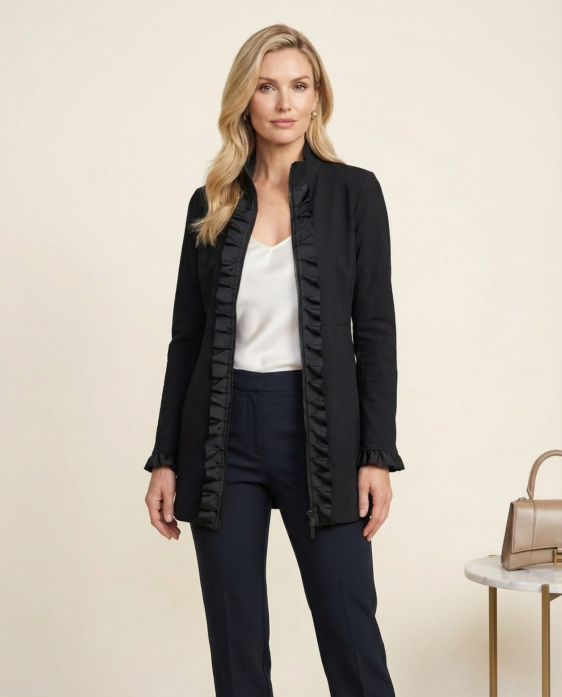 Woman wearing a black ruffled jacket with a white top and dark pants on a beige background.