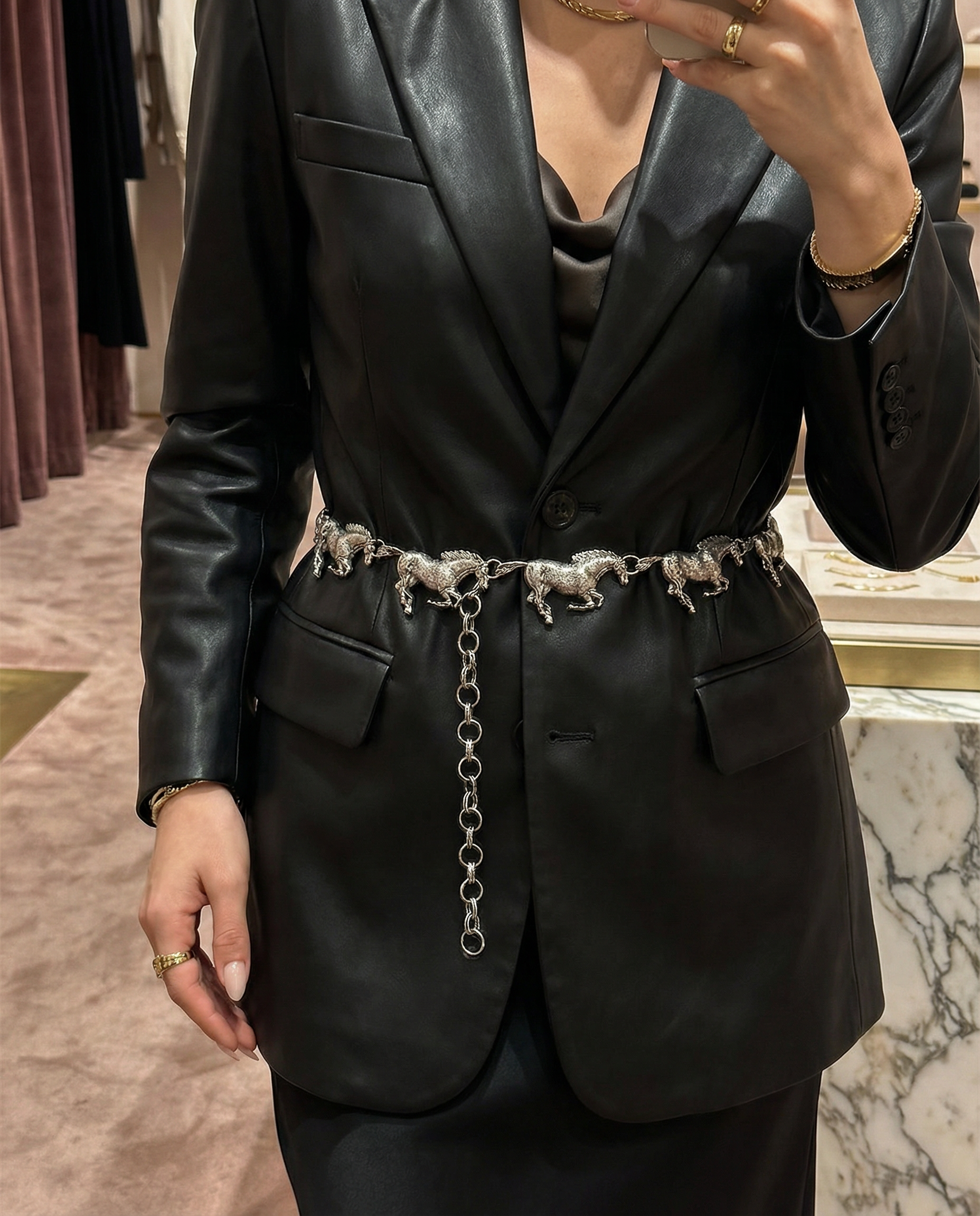 Person wearing a black blazer with a decorative belt in front of a mirror.